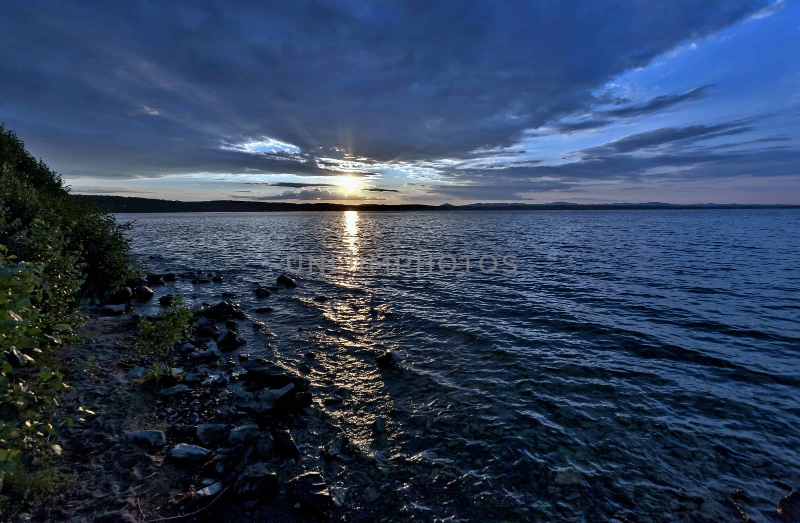 the evening sky over the lake, silhouettes of clouds illuminated by the sun