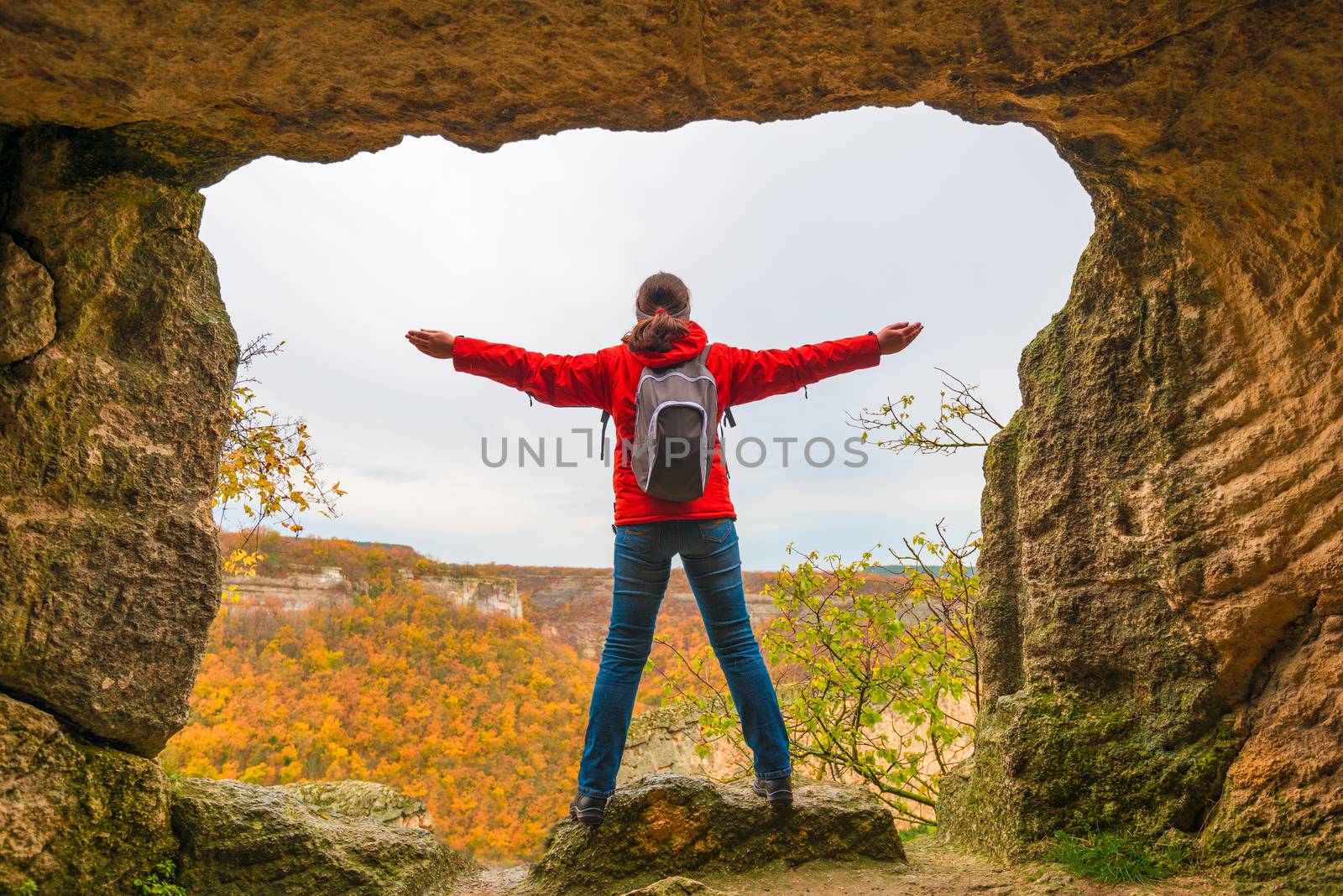 A tourist with a backpack looks from the mountain to a beautiful autumn forest, arms outstretched