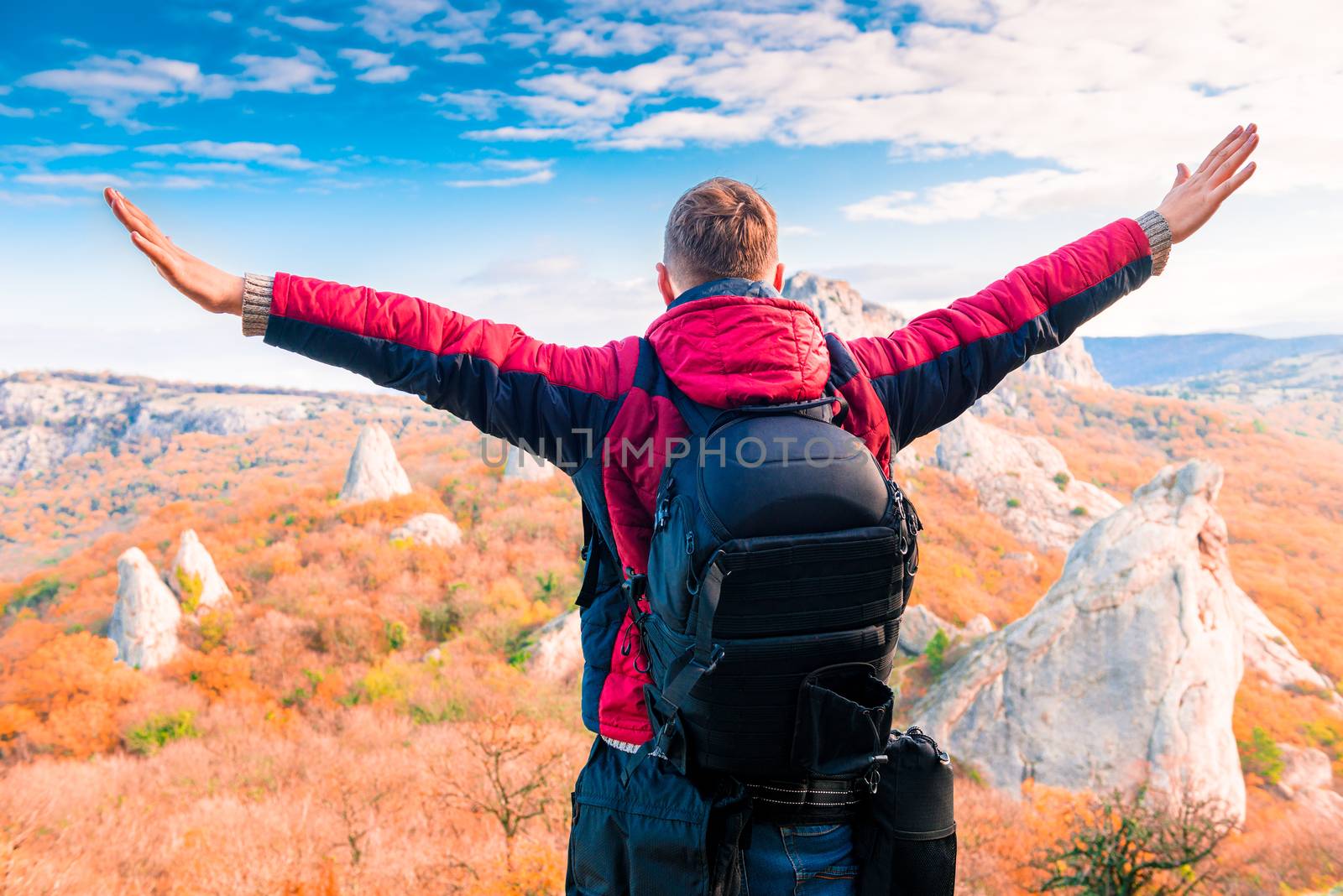 Man Tourist with a backpack with open arms enjoying the autumn landscape in the mountains