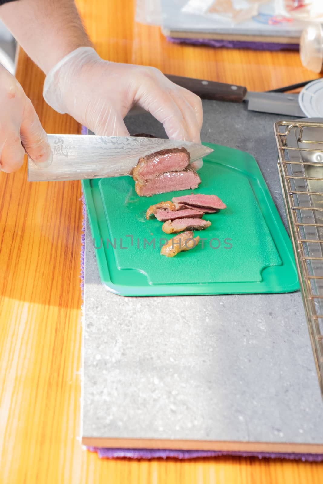 Chef in transparent gloves cuts juicy meat steak on a green Board with a knife, close-up. by rdv27