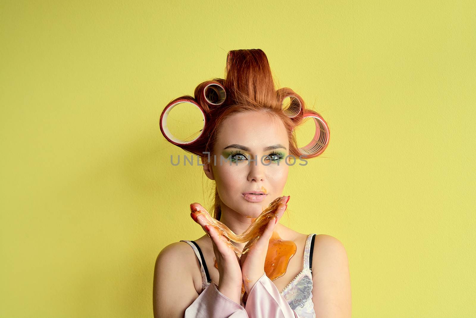 Young redhead woman with shugaring paste on her hands, face, body and chest. Young redhead woman with hair curlers. Advertising concept of shugaring paste. Skin care concept with copyspace.