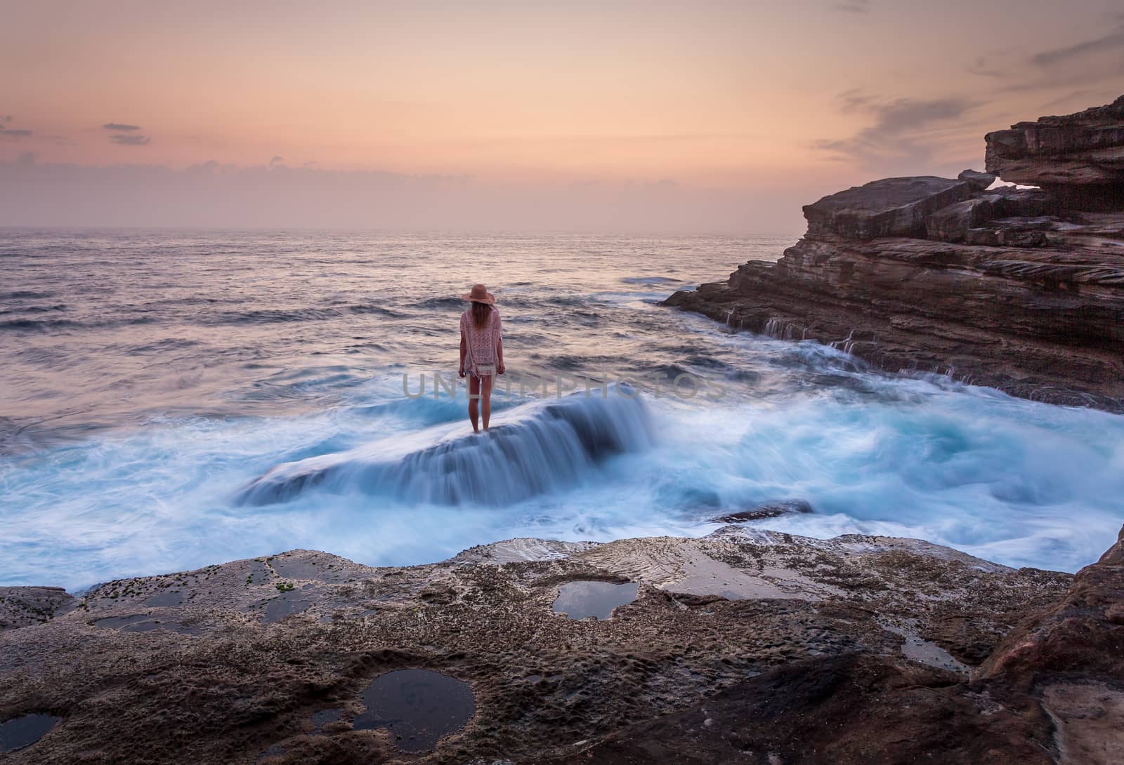 Woman stands on the shipwreck rock with ocean awash overflows at low tide with pretty dawn skies. Life, courage, determination