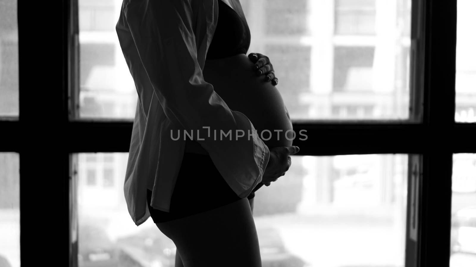 Pregnant woman standing by window - black and white silhouette