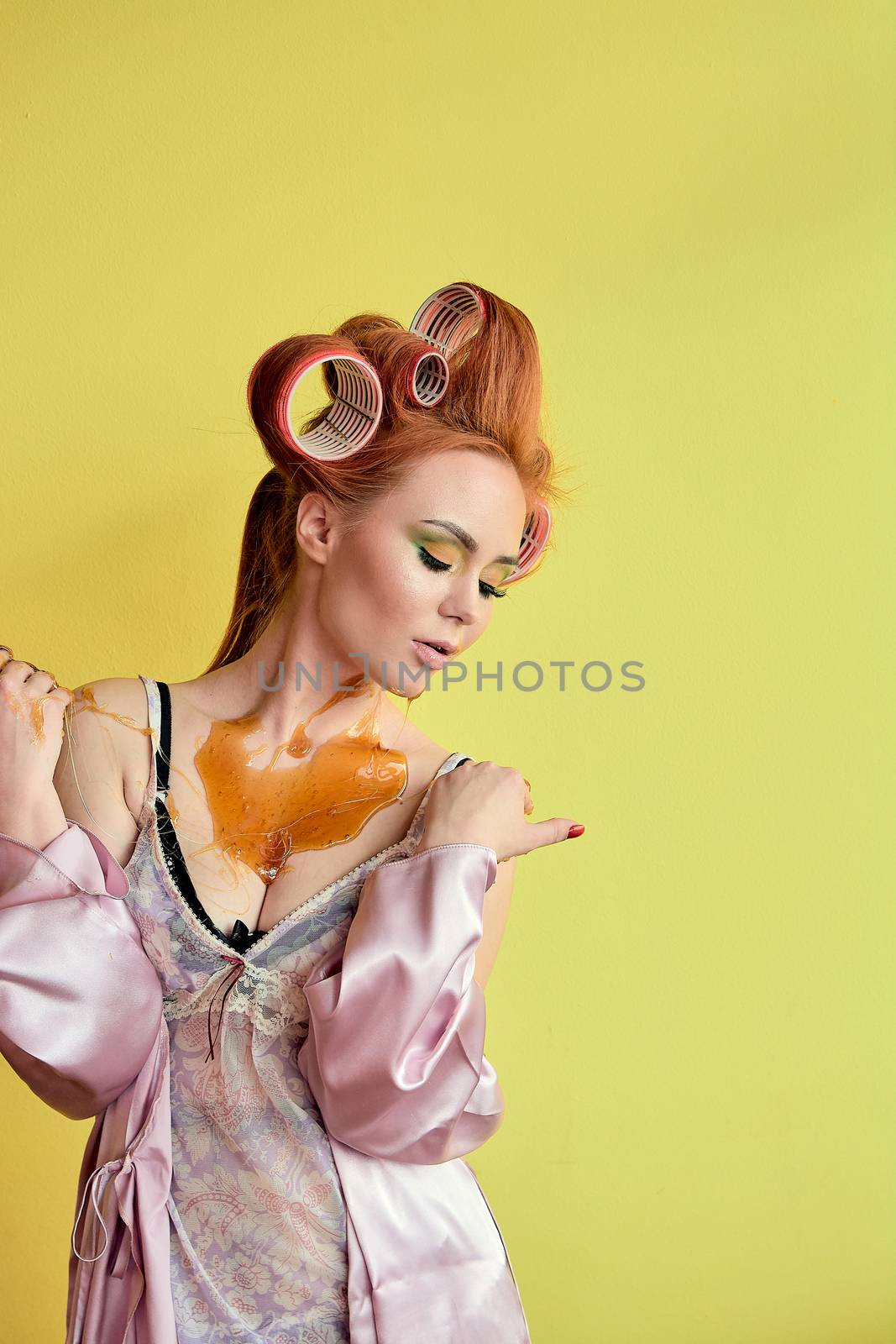 Young redhead woman with shugaring paste on her hands, face, body and chest. Young redhead woman with hair curlers. Advertising concept of shugaring paste. Skin care concept with copyspace.