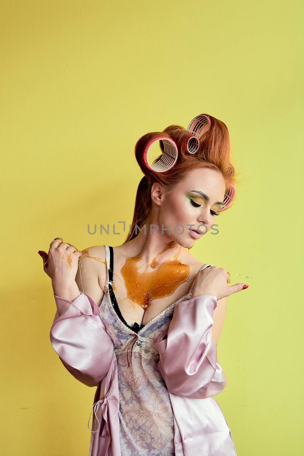 Young redhead woman with shugaring paste on her hands, face, body and chest. Young redhead woman with hair curlers. Advertising concept of shugaring paste. Skin care concept with copyspace.