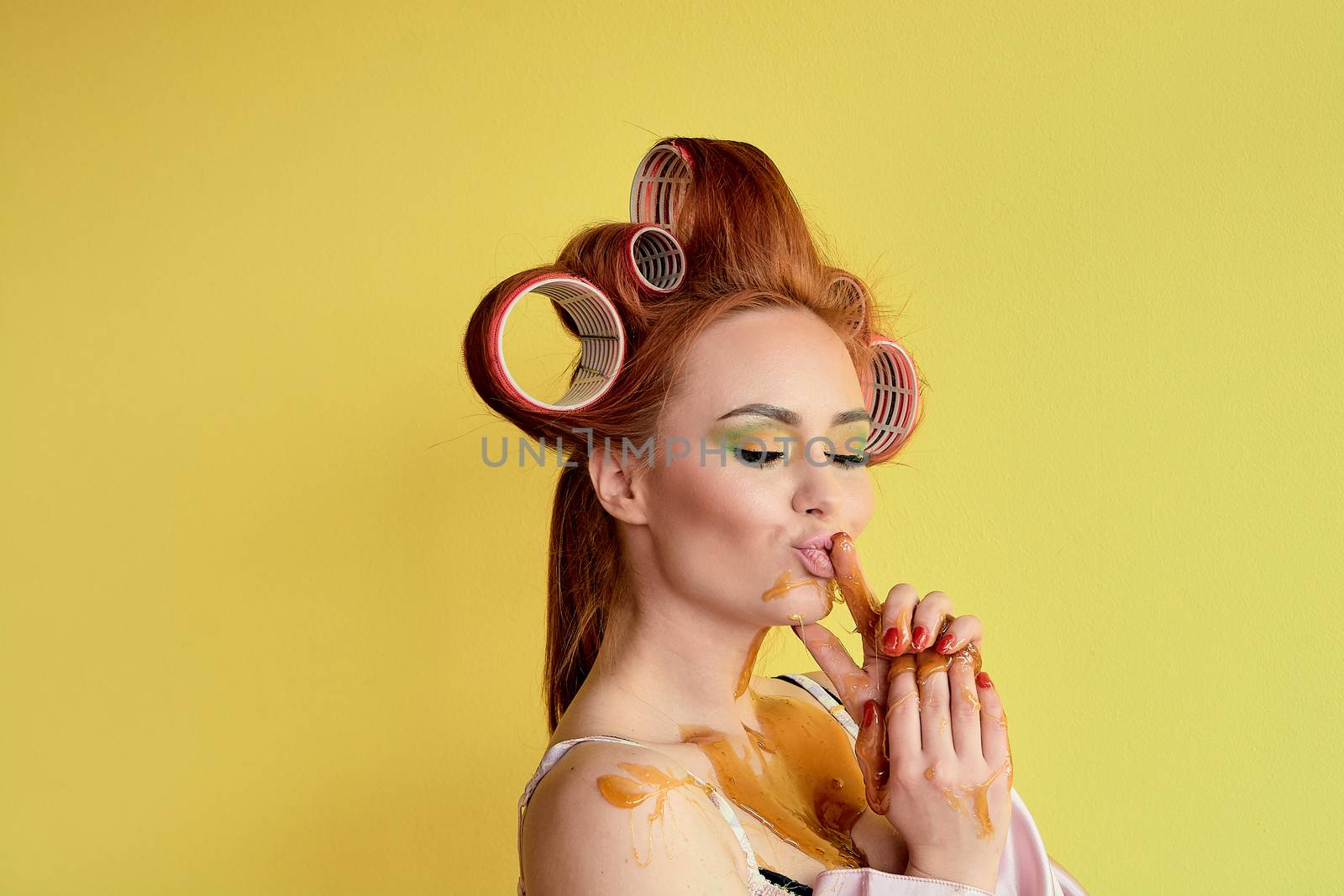 Young redhead woman with shugaring paste on her hands, face, body and chest. Young redhead woman with hair curlers. Advertising concept of shugaring paste. Skin care concept with copyspace.