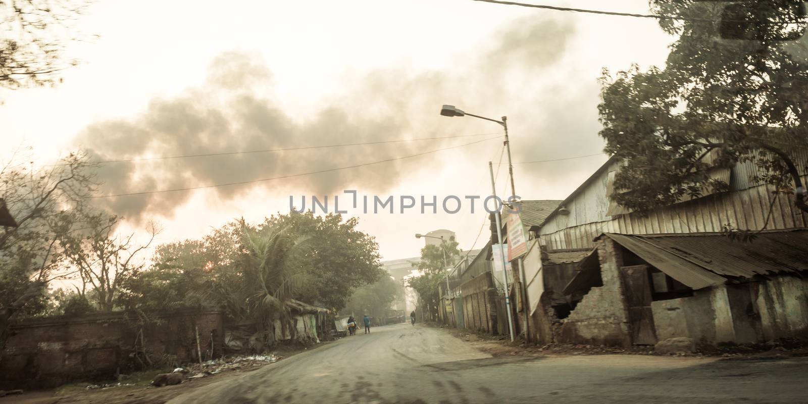 Kolkata, India - May 1, 2018 - Burning fire from garbage heap in industrial area, causing a large flame and smoke in the air over dramatic sky background. Firemen rush to help prevent spread of fire. by sudiptabhowmick