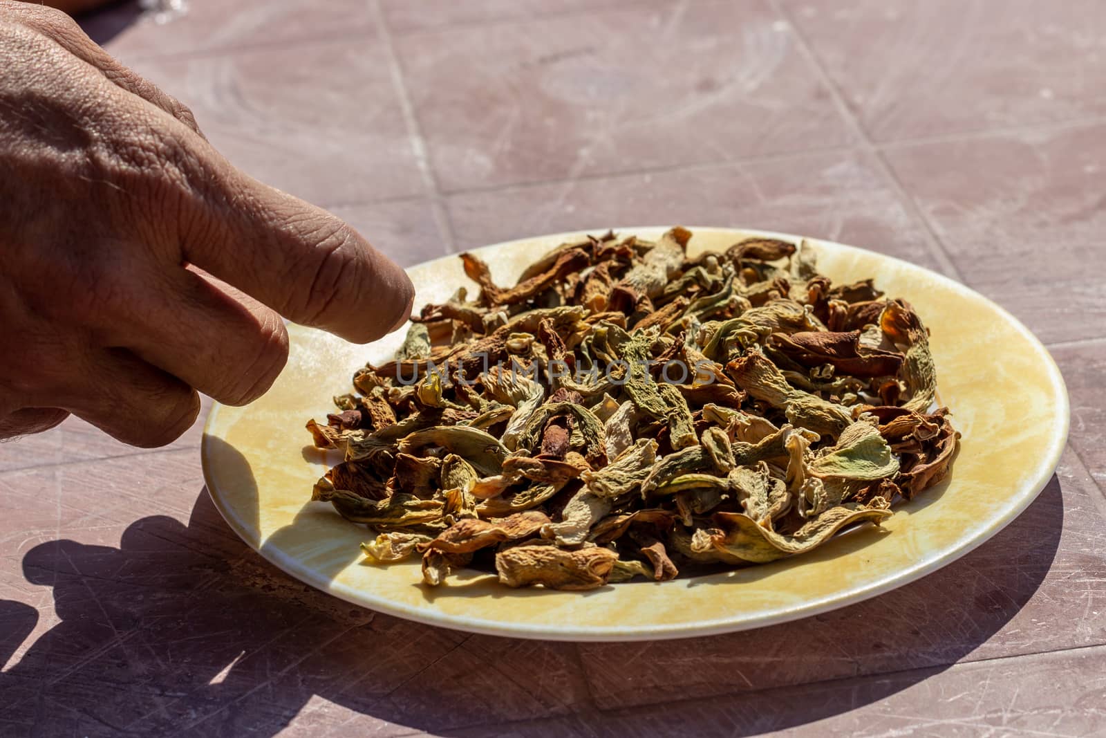 a side view shoot to dried peppers on plate with a person touching it. photo has taken at a village at turkey.