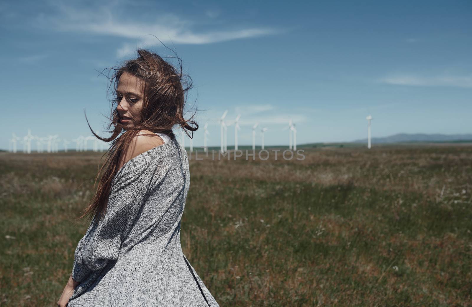 Woman with long tousled hair next to the wind turbine with the wind blowing