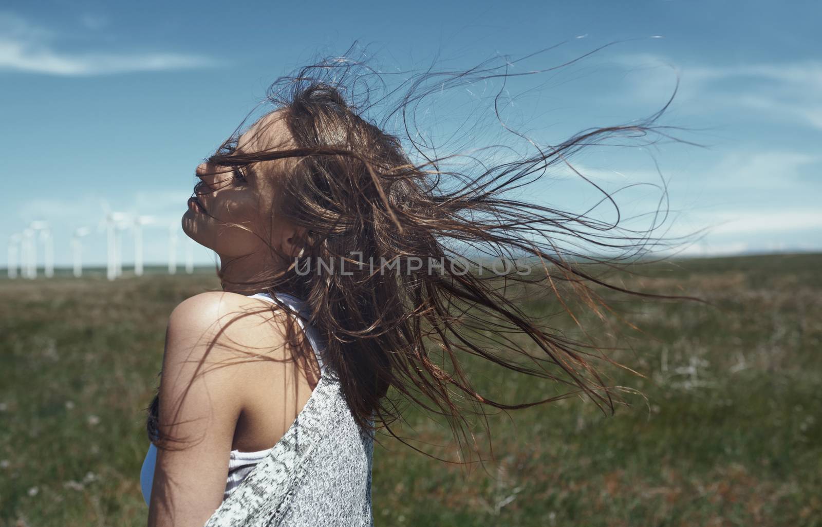 Woman with long tousled hair next to the wind turbine with the wind blowing