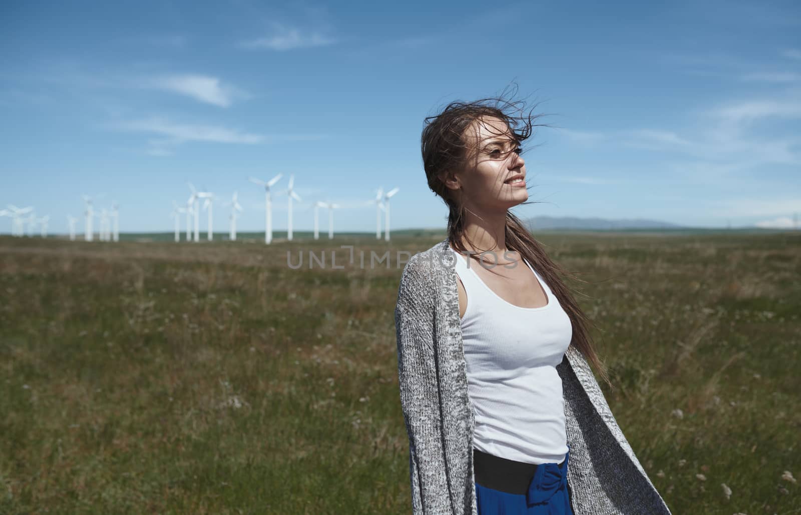 Woman with long tousled hair next to the wind turbine with the wind blowing