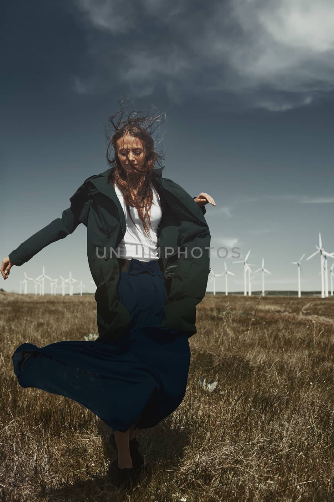 Woman with long tousled hair next to the wind turbine with the wind blowing