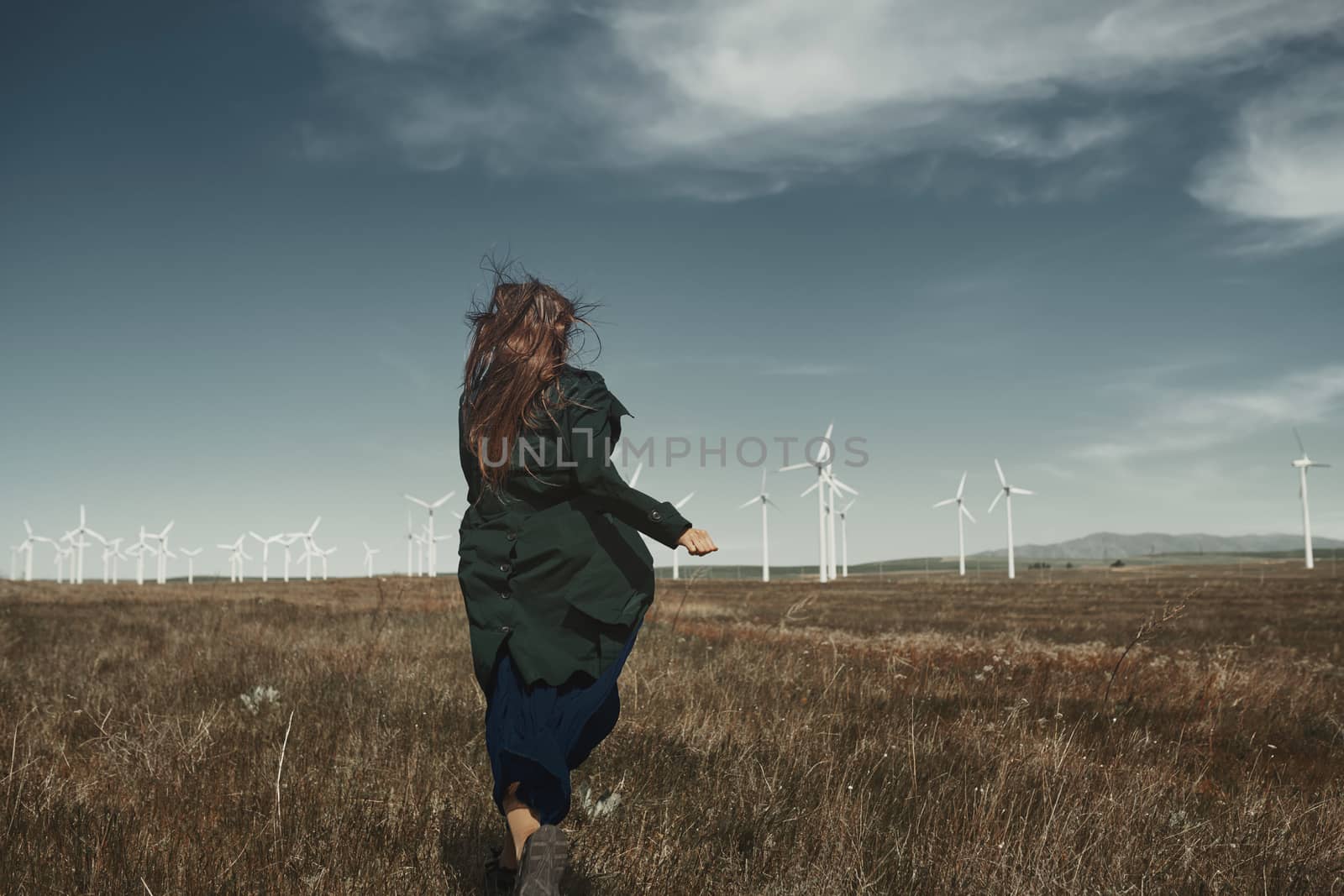 Woman with long tousled hair next to the wind turbine with the wind blowing