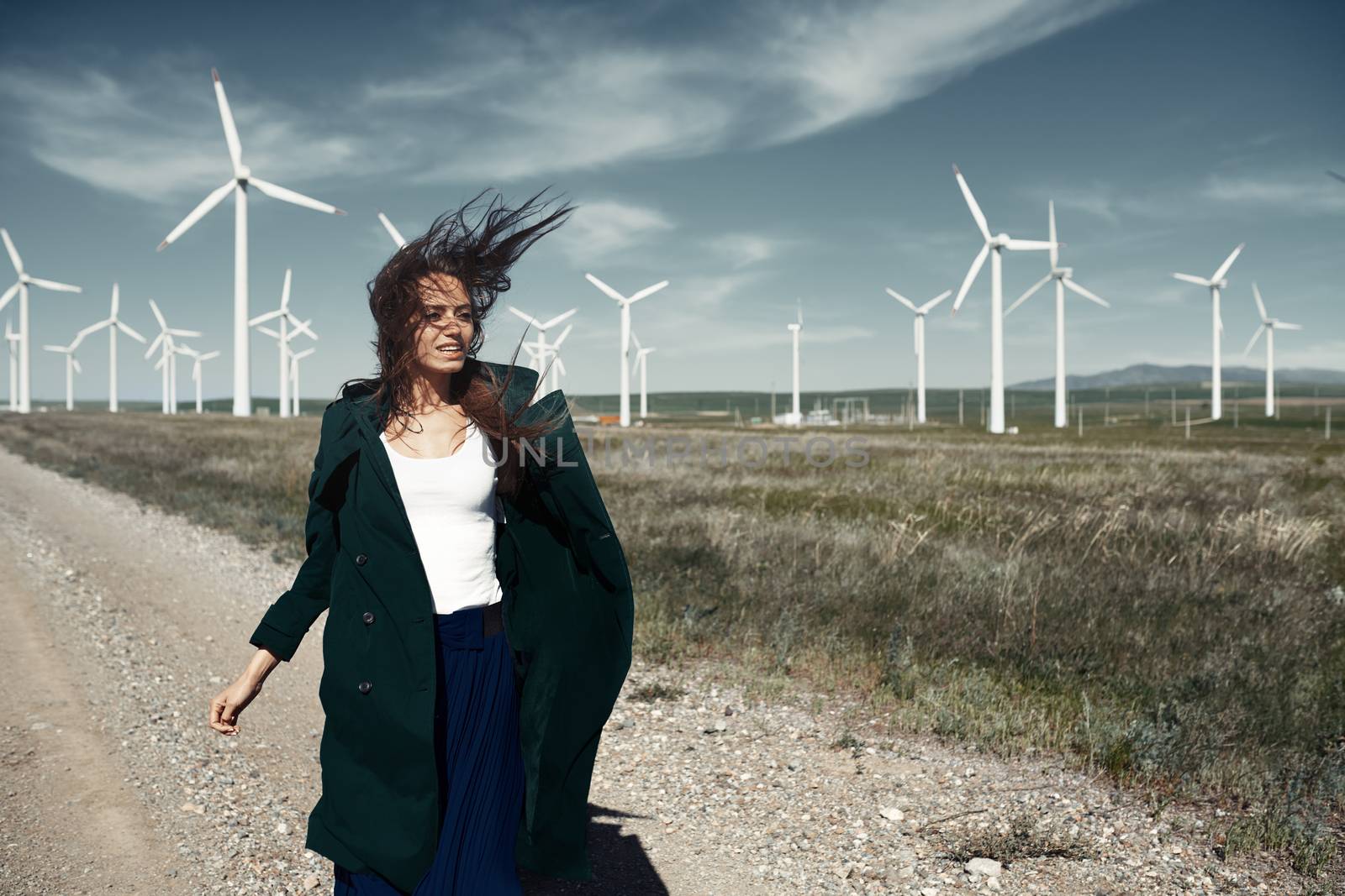 Woman with long tousled hair next to the wind turbine with the wind blowing