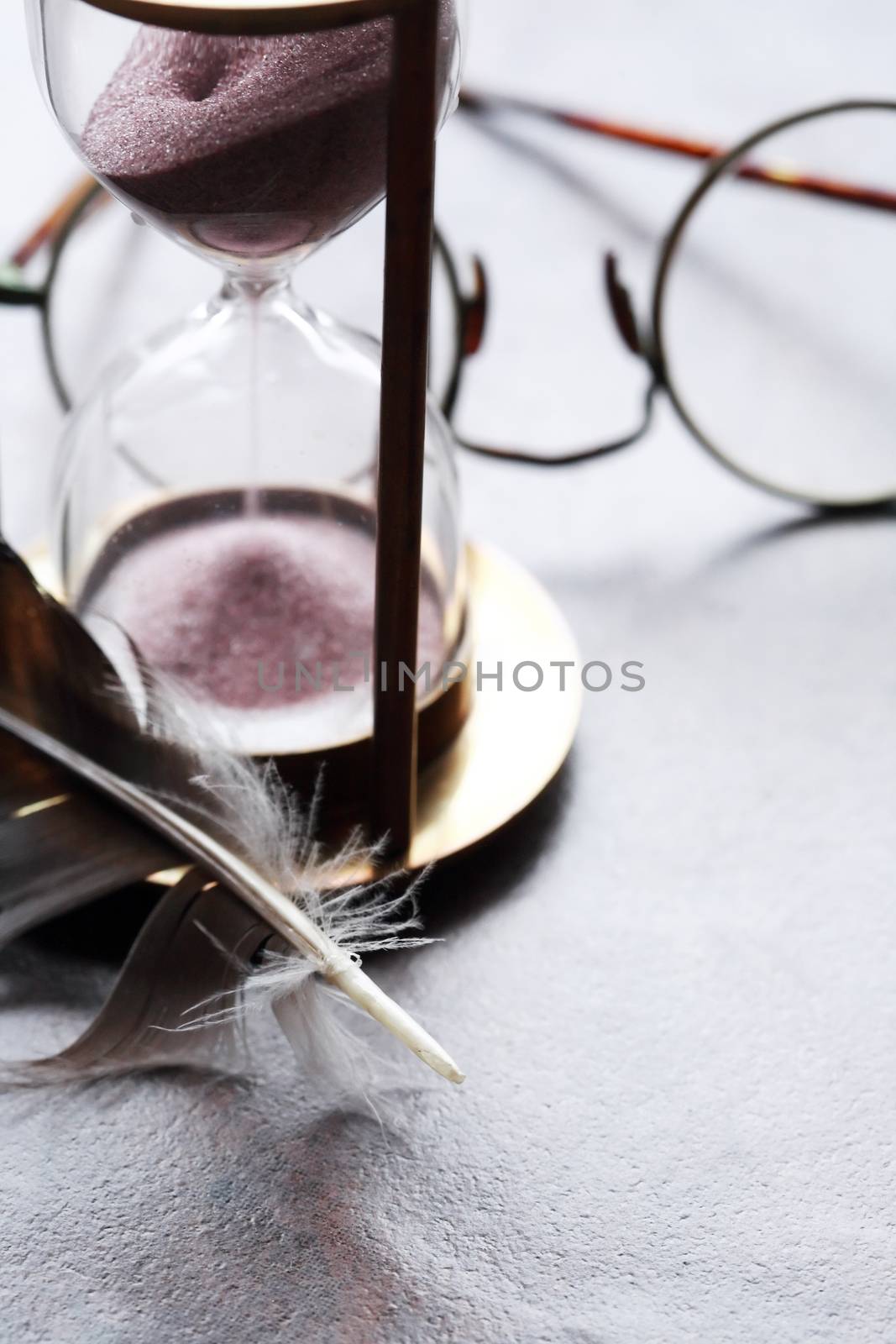 Vintage still life with hourglass near feather and old spectacles