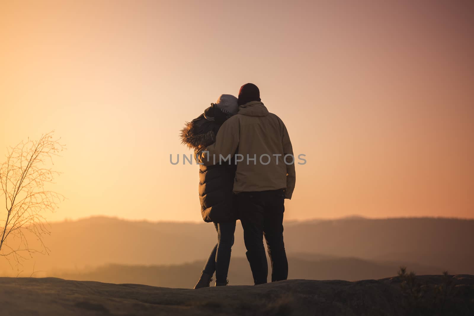 Silhouettes of a man and woman on mountain peak at sunrise. Landscape with silhouette of lovers against colorful sky