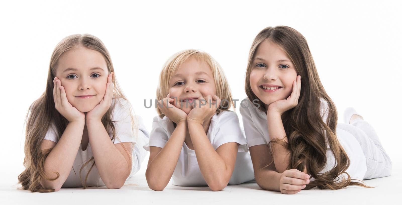 Three happy children laying on floor resting head on hands isolated on white background