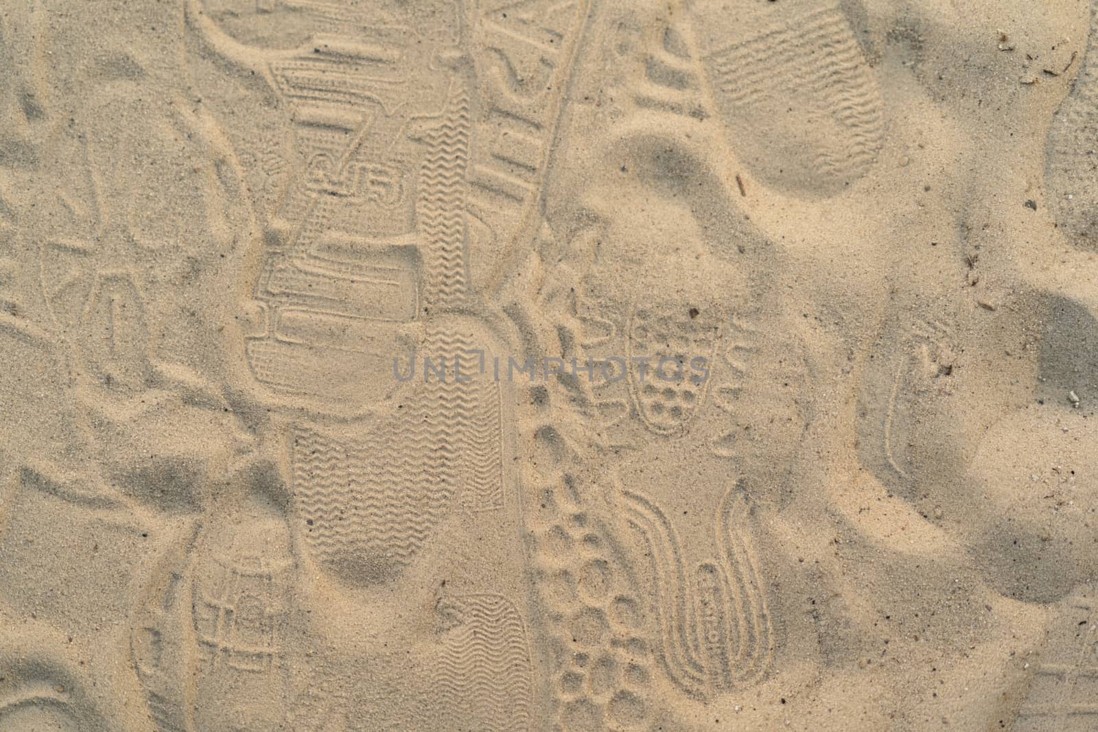 Sand on the beach with footprints and shoes. Many footprints with shoes and without shoes.