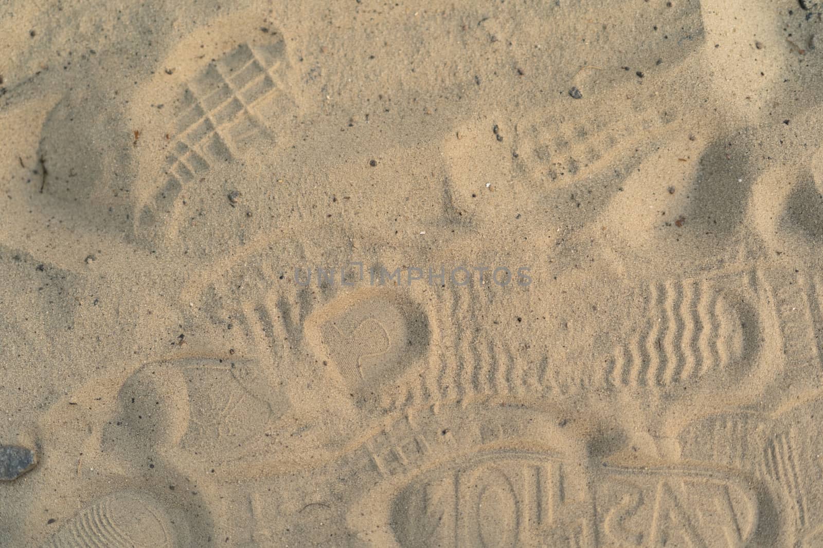 Sand on the beach with footprints and shoes. Many footprints with shoes and without shoes. by alexsdriver