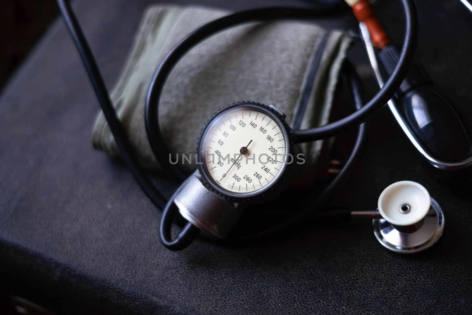 Analog tonometer with cuff and phonendoscope on old suitcase. Close up view and blurred background. Underexposed photo.