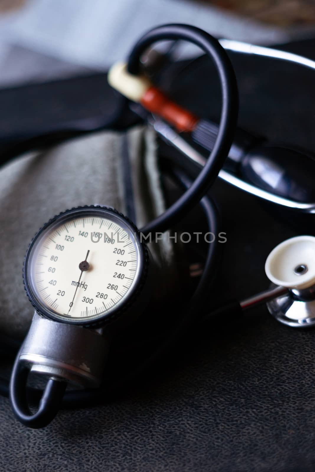 Analog tonometer with cuff and phonendoscope on old suitcase. Close up view and blurred background. Underexposed photo. by alexsdriver