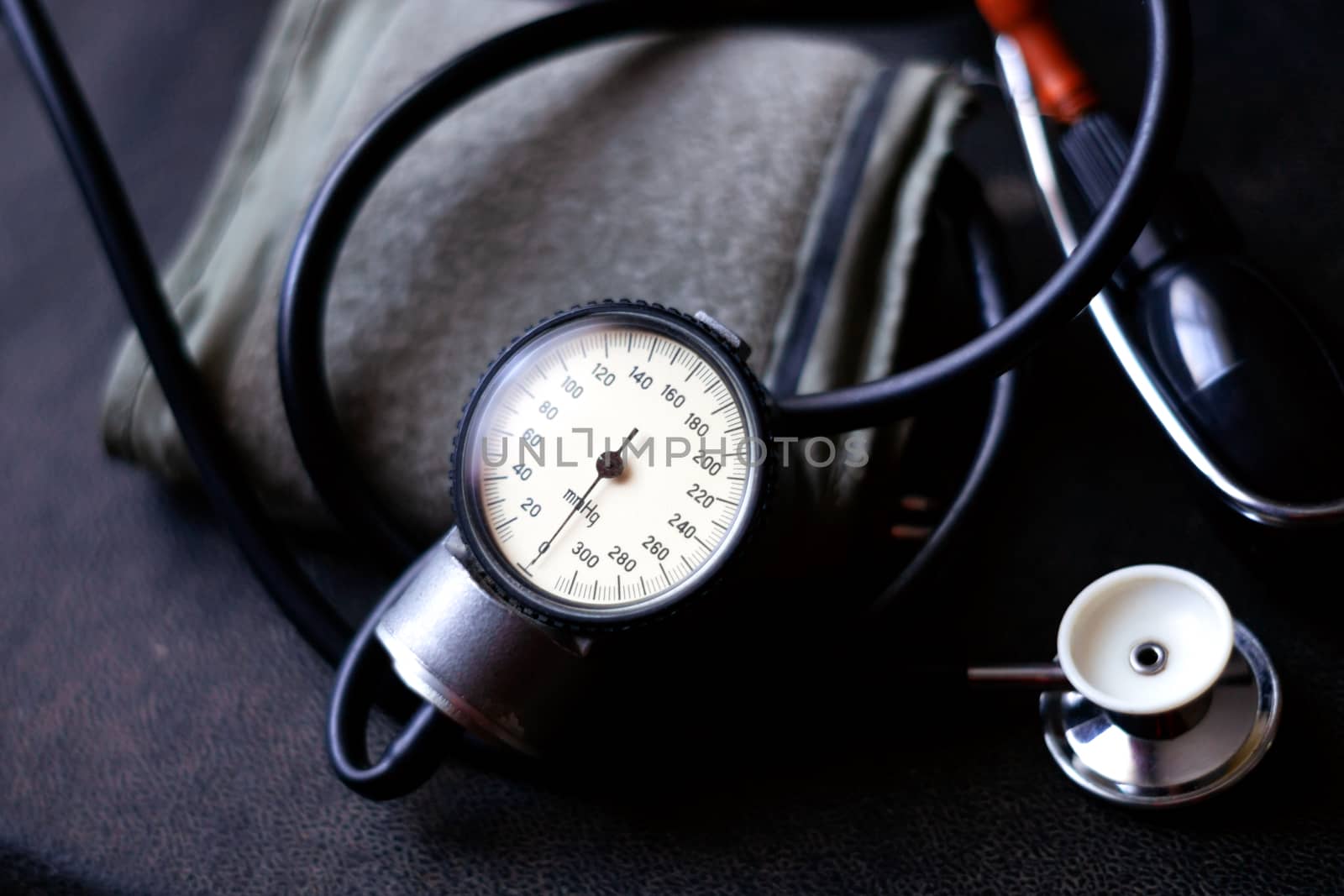 Analog tonometer with cuff and phonendoscope on old suitcase. Close up view and blurred background. Underexposed photo. by alexsdriver