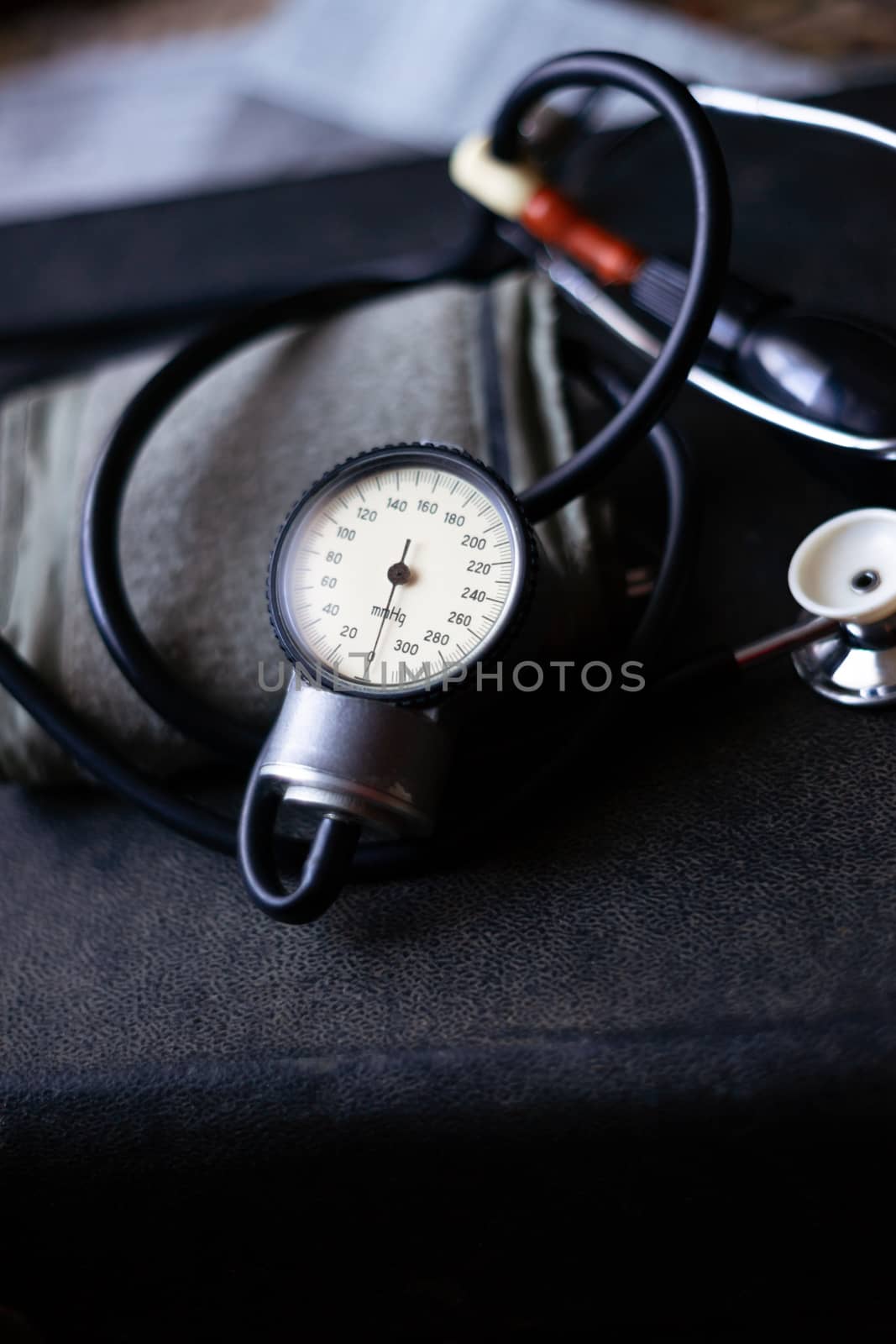 Analog tonometer with cuff and phonendoscope on old suitcase. Close up view and blurred background. Underexposed photo.