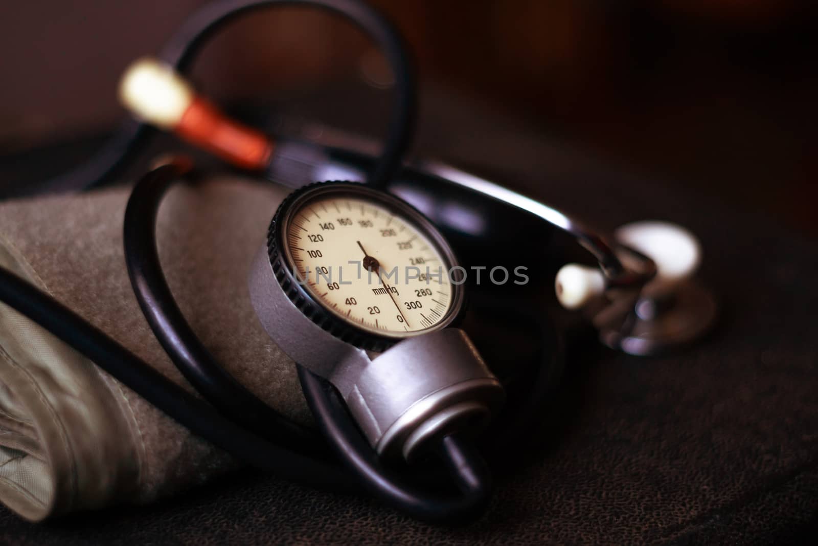 Analog tonometer with cuff and phonendoscope on old suitcase. Close up view and blurred background. Underexposed photo.