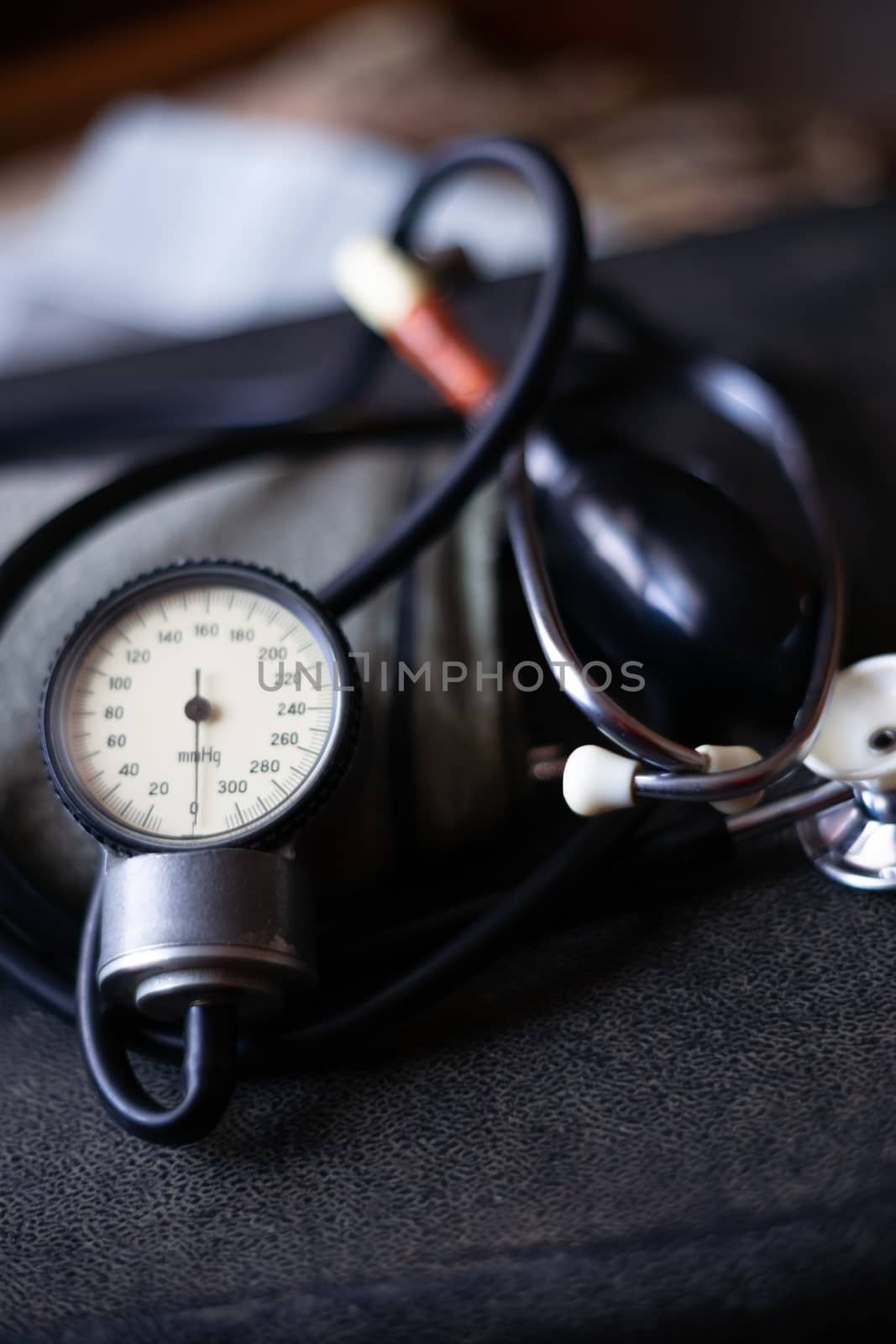 Analog tonometer with cuff and phonendoscope on old suitcase. Close up view and blurred background. Underexposed photo. by alexsdriver