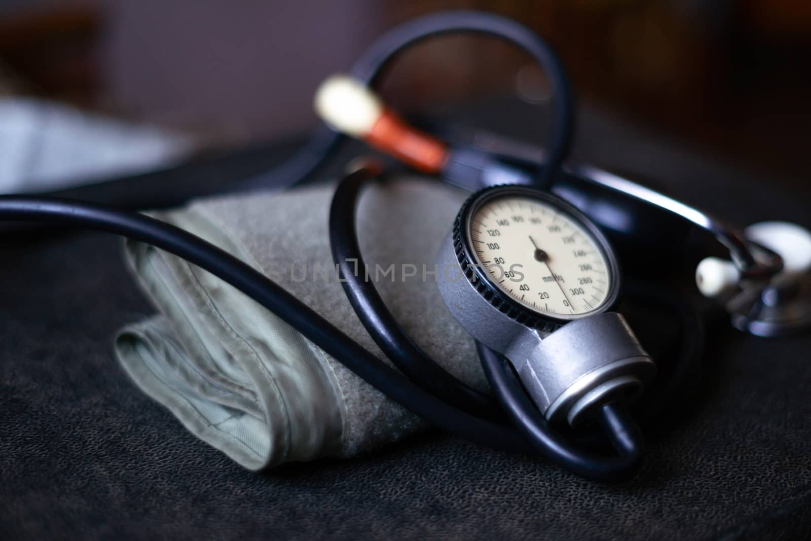 Analog tonometer with cuff and phonendoscope on old suitcase. Close up view and blurred background. Underexposed photo. by alexsdriver