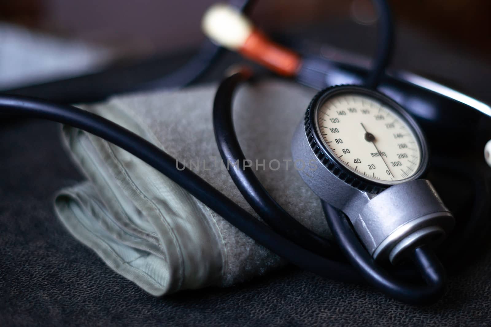 Analog tonometer with cuff and phonendoscope on old suitcase. Close up view and blurred background. Underexposed photo.