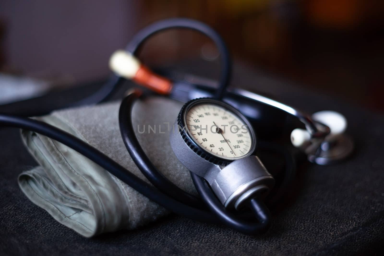 Analog tonometer with cuff and phonendoscope on old suitcase. Close up view and blurred background. Underexposed photo.