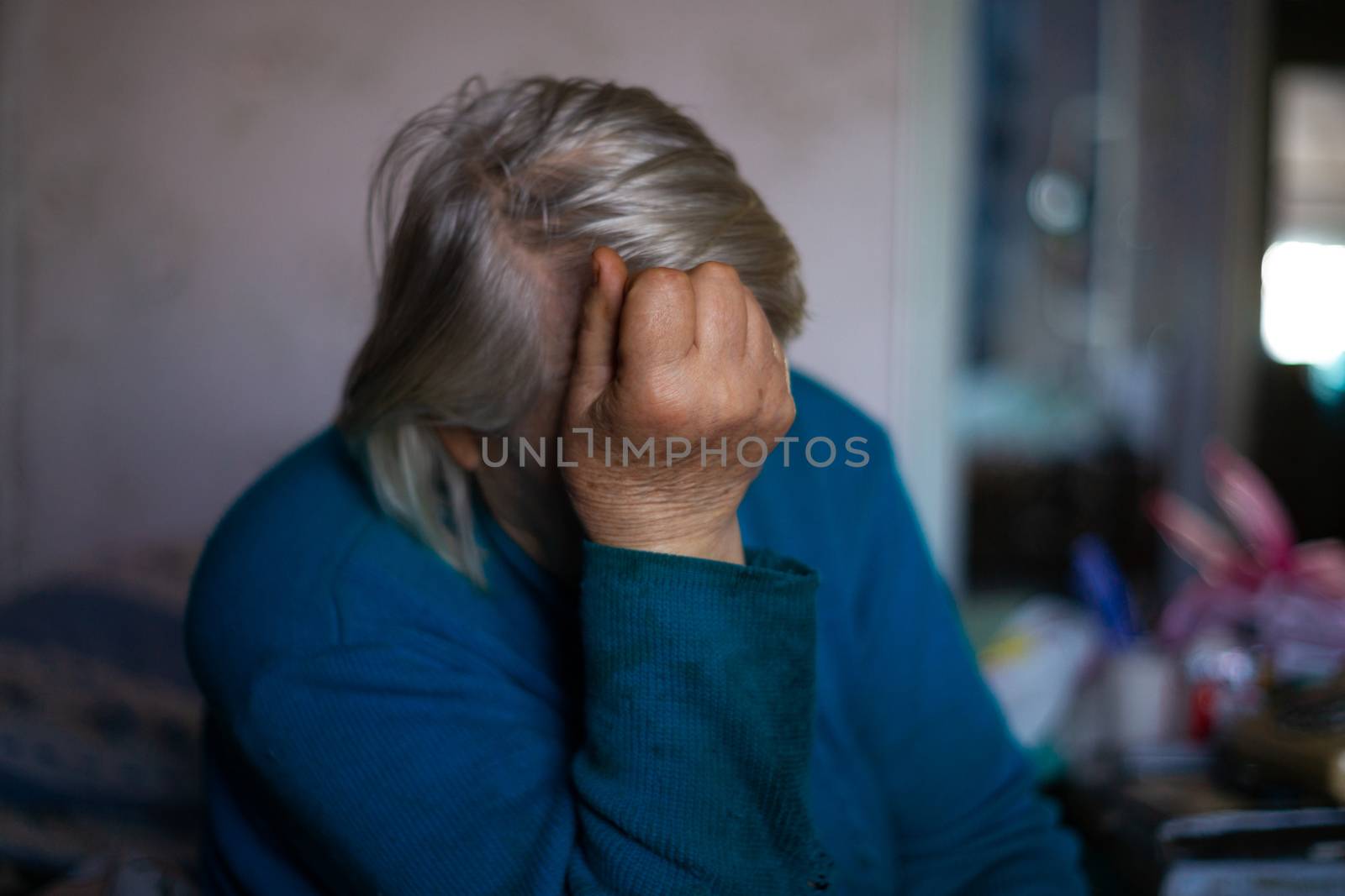 Old poor gray hair woman covered her face with her hand. Woman is sad. Poor life in village. Old age not good. Low-light photo.