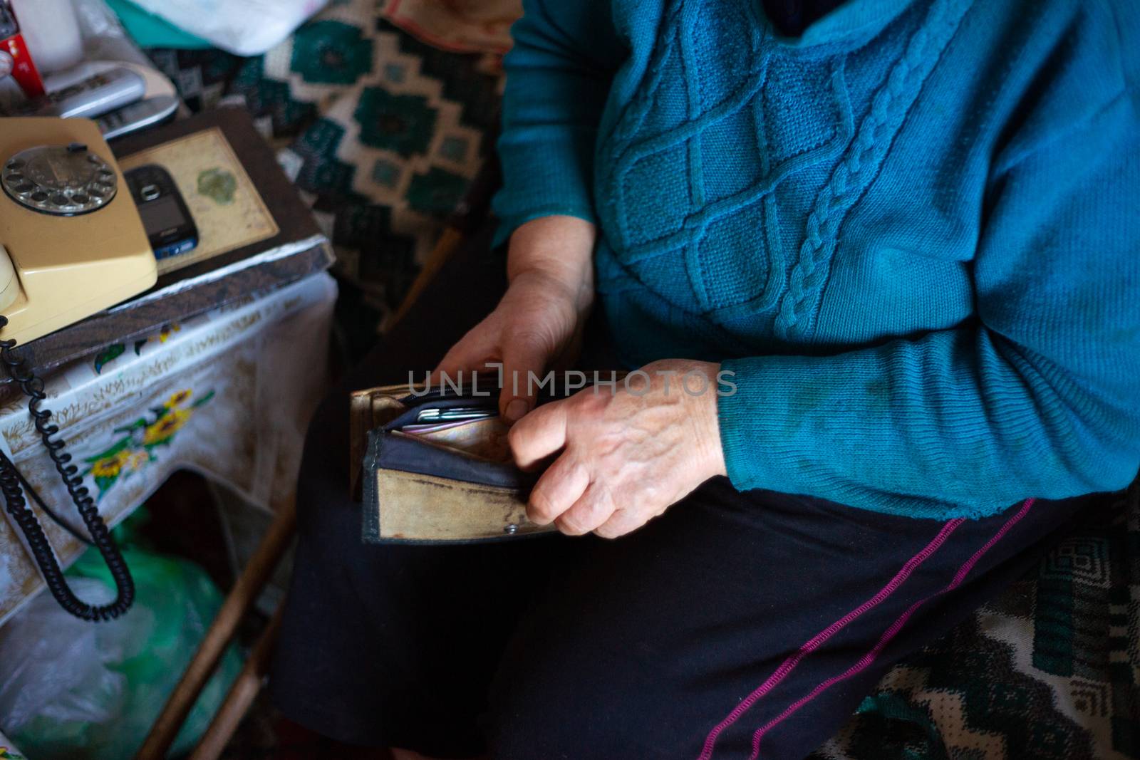 Old poor gray hair woman holds Ukrainian hryvna money in her hands. Woman is sad. Poor life in village. Old age not good. Low-light photo. by alexsdriver