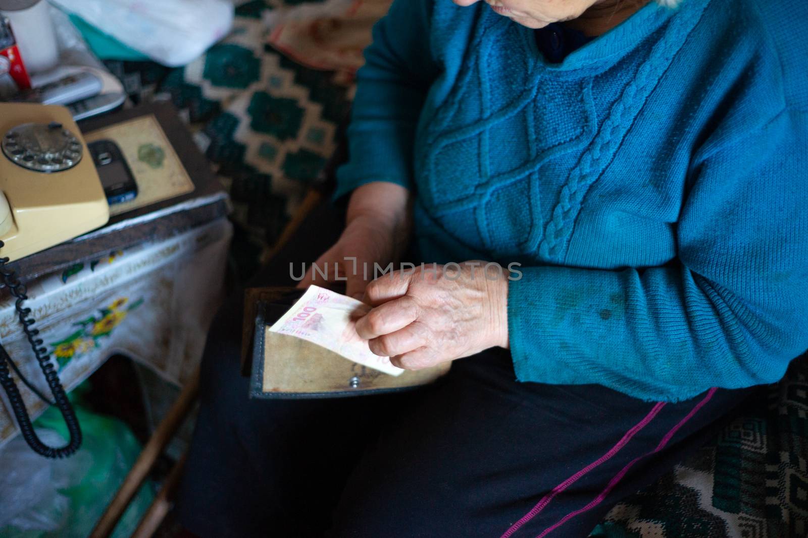 Old poor gray hair woman holds Ukrainian hryvna money in her hands. Woman is sad. Poor life in village. Old age not good. Low-light photo. by alexsdriver