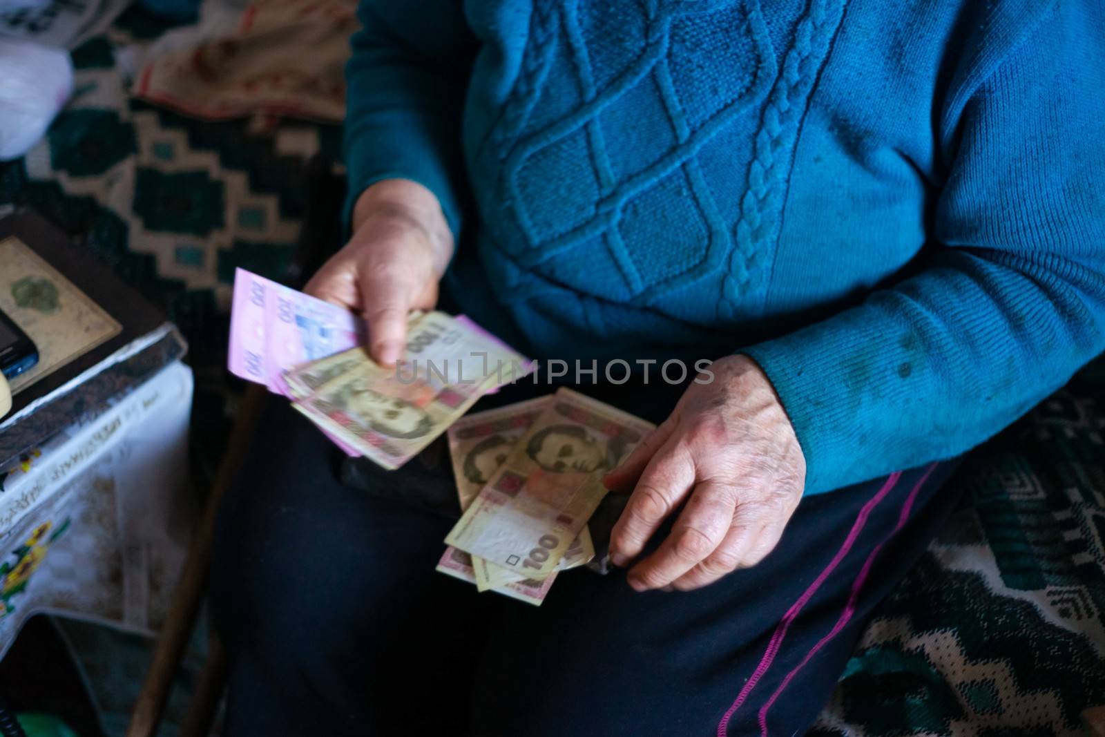 Old poor gray hair woman holds Ukrainian paper money in her hands. Woman is sad. Poor life in village. Old age not good. Low-light photo. by alexsdriver