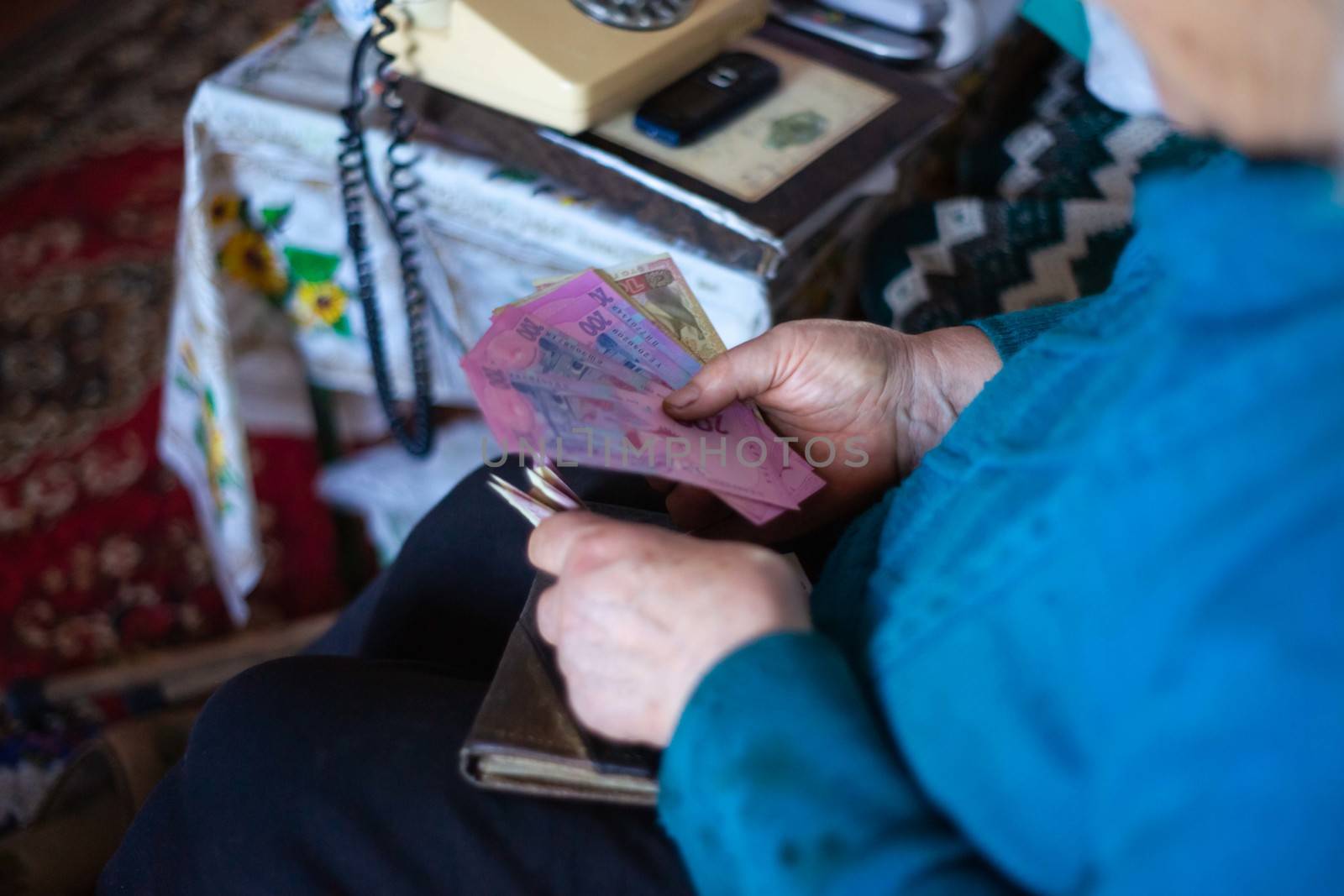 Old poor gray hair woman holds Ukrainian paper money in her hands. Woman is sad. Poor life in village. Old age not good. Low-light photo. by alexsdriver