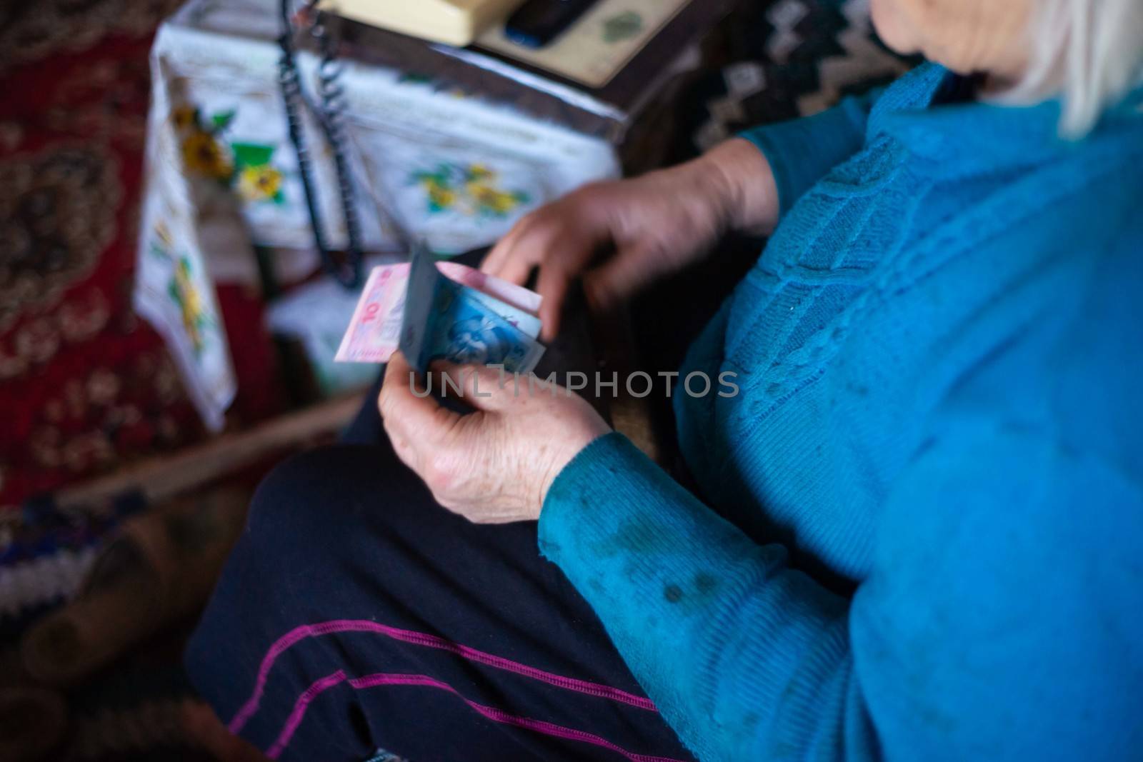 Old poor gray hair woman holds Ukrainian paper money in her hands. Woman is sad. Poor life in village. Old age not good. Low-light photo. by alexsdriver