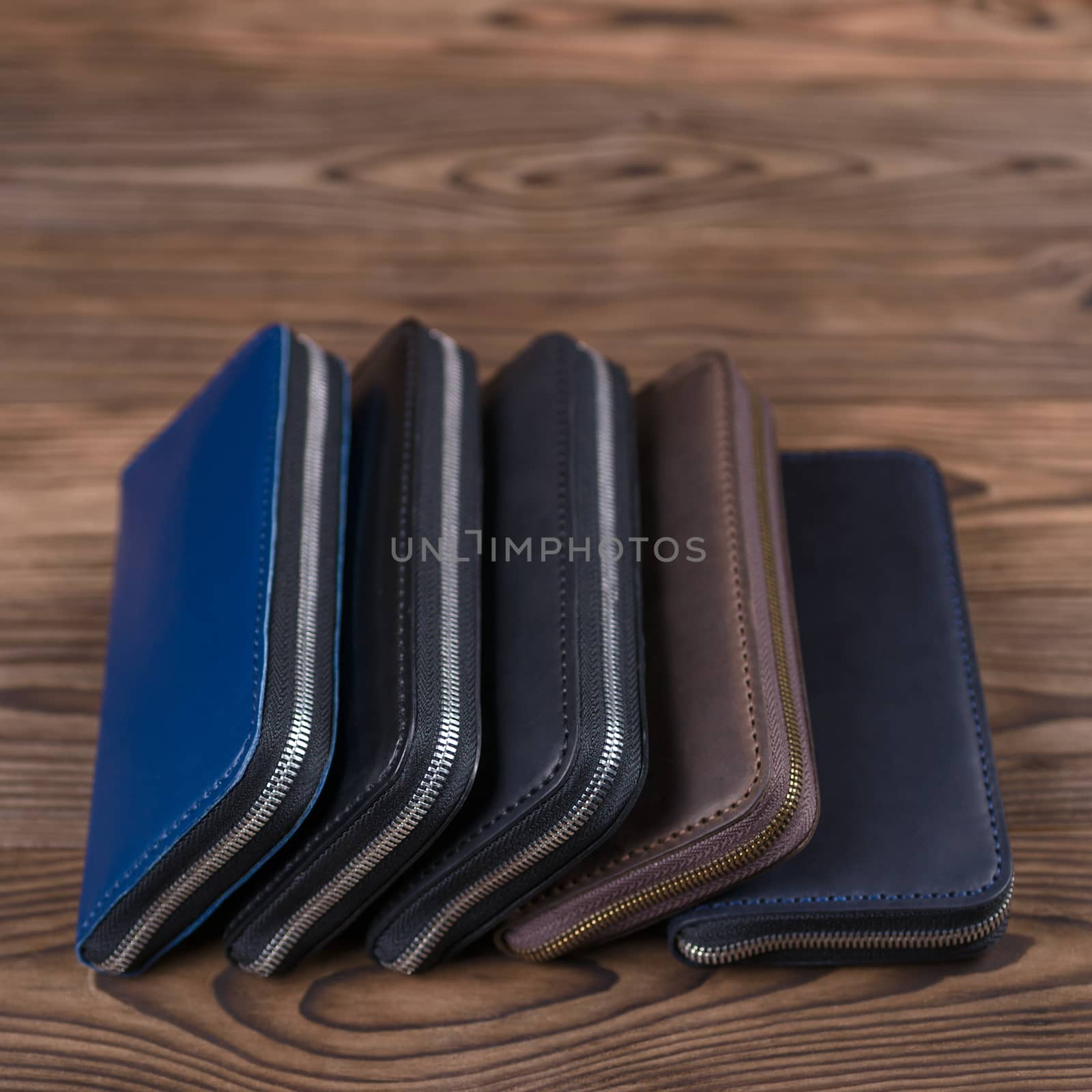 Five handmade leather porte-monnaie lies on wooden textured background.  Side view. Stock photo of luxury accessories with blurred background..