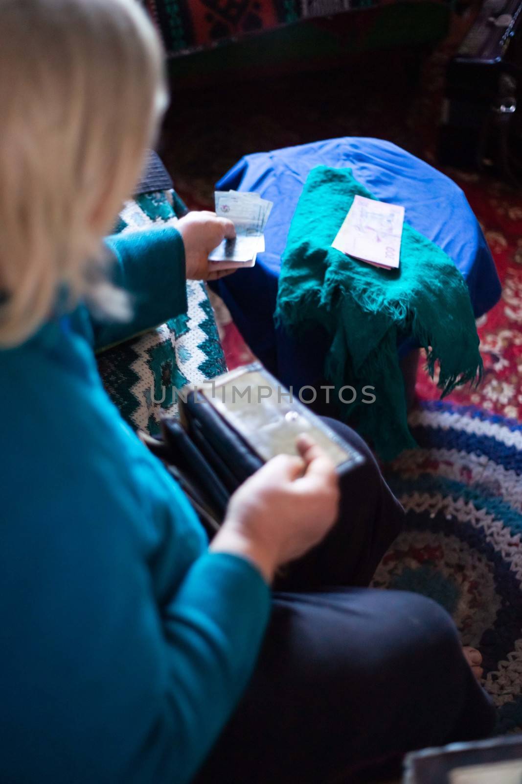 Old poor gray hair woman holds Ukrainian paper money in her hands. Woman is sad. Poor life in village. Old age not good. Low-light photo.