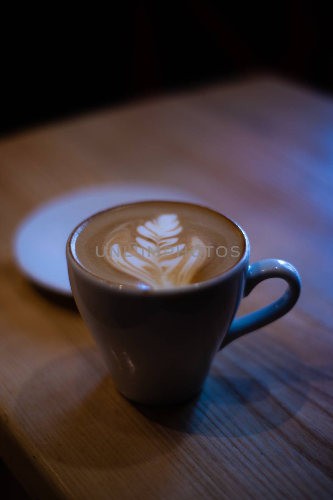 A low light shot of cappuccino cup with latte art on wooden table. by alexsdriver