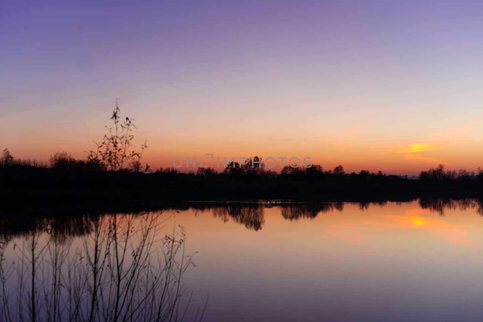Blue time evening sky landscape with trees and lake in foreground. Blue time sunset. Perfect teal and orange colors. Low-light underexposed photo. by alexsdriver