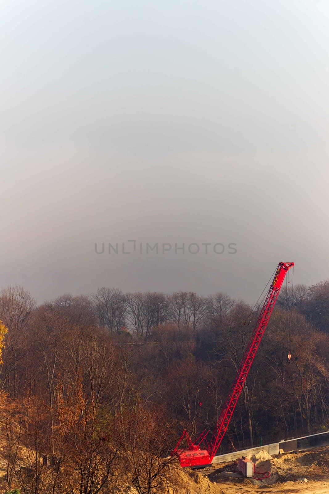 Construction process with construction automotive cranes with red and white gibbets. Autumn fog and river bridge  on blurred background. Forest around cranes.