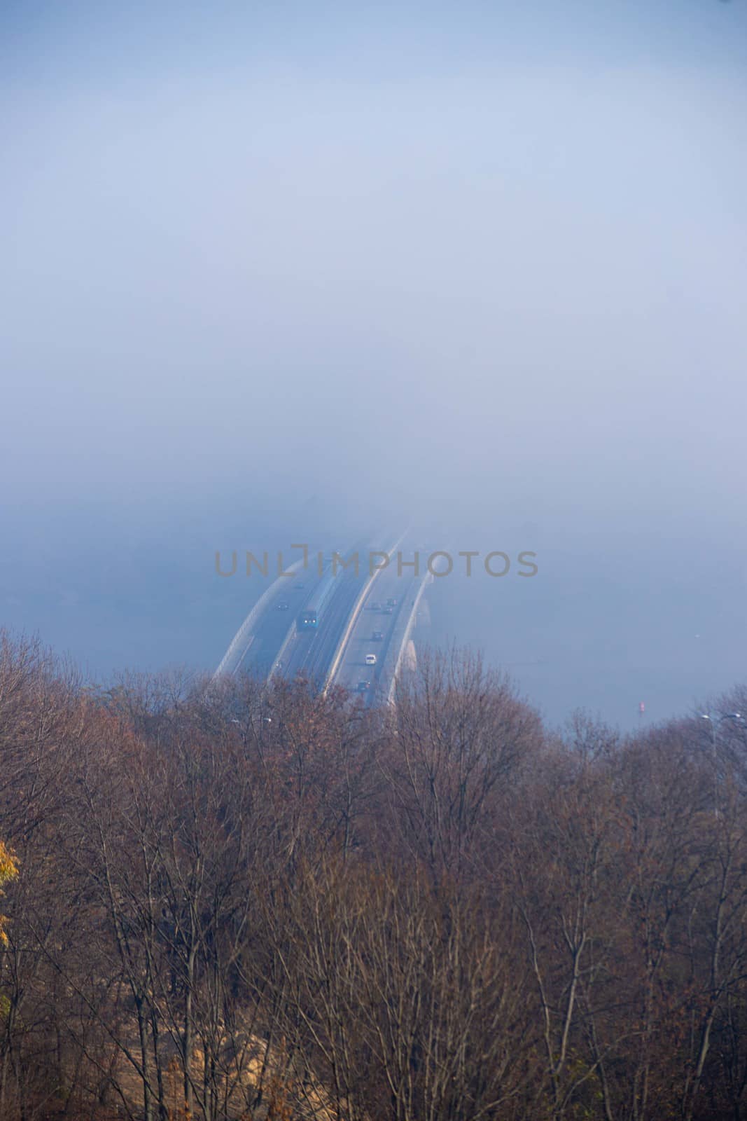 Autumn fog and river steel bridge with subway train on blurred background. Forest in foreground.