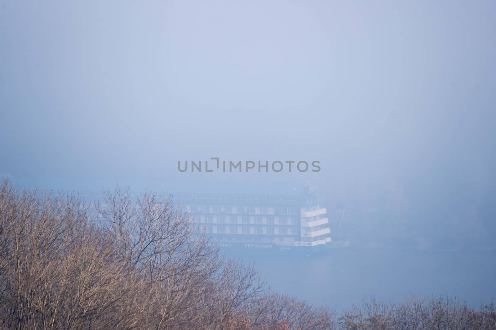 Autumn fog and big floating hotel in river on blurred background. Forest in foreground.