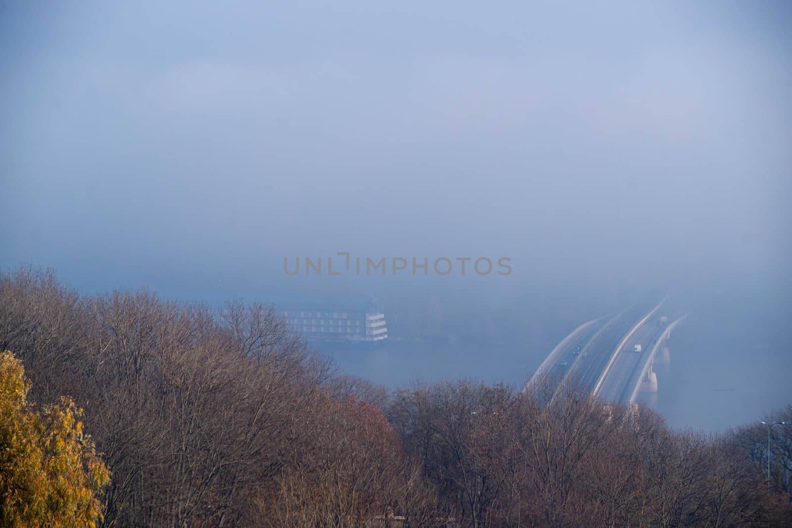 Autumn fog and river steel bridge with subway train on blurred background. Big floating boat hotel in river. Forest in foreground.