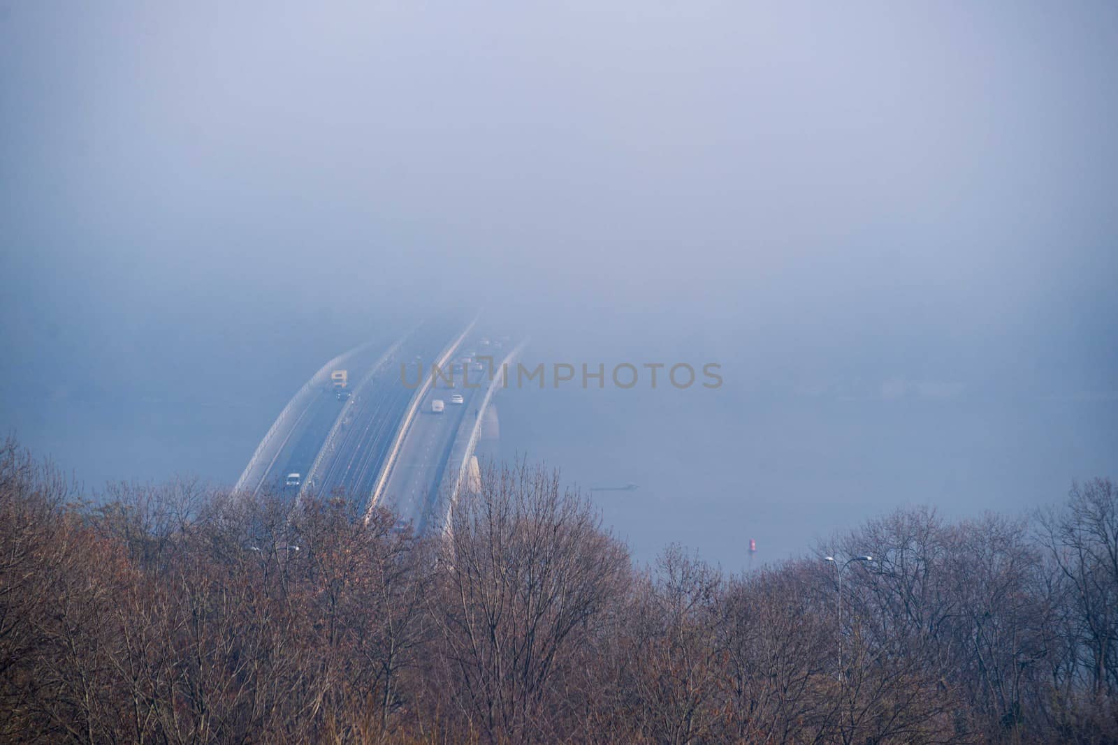 Autumn fog and river steel bridge with subway train on blurred background. Forest in foreground.
