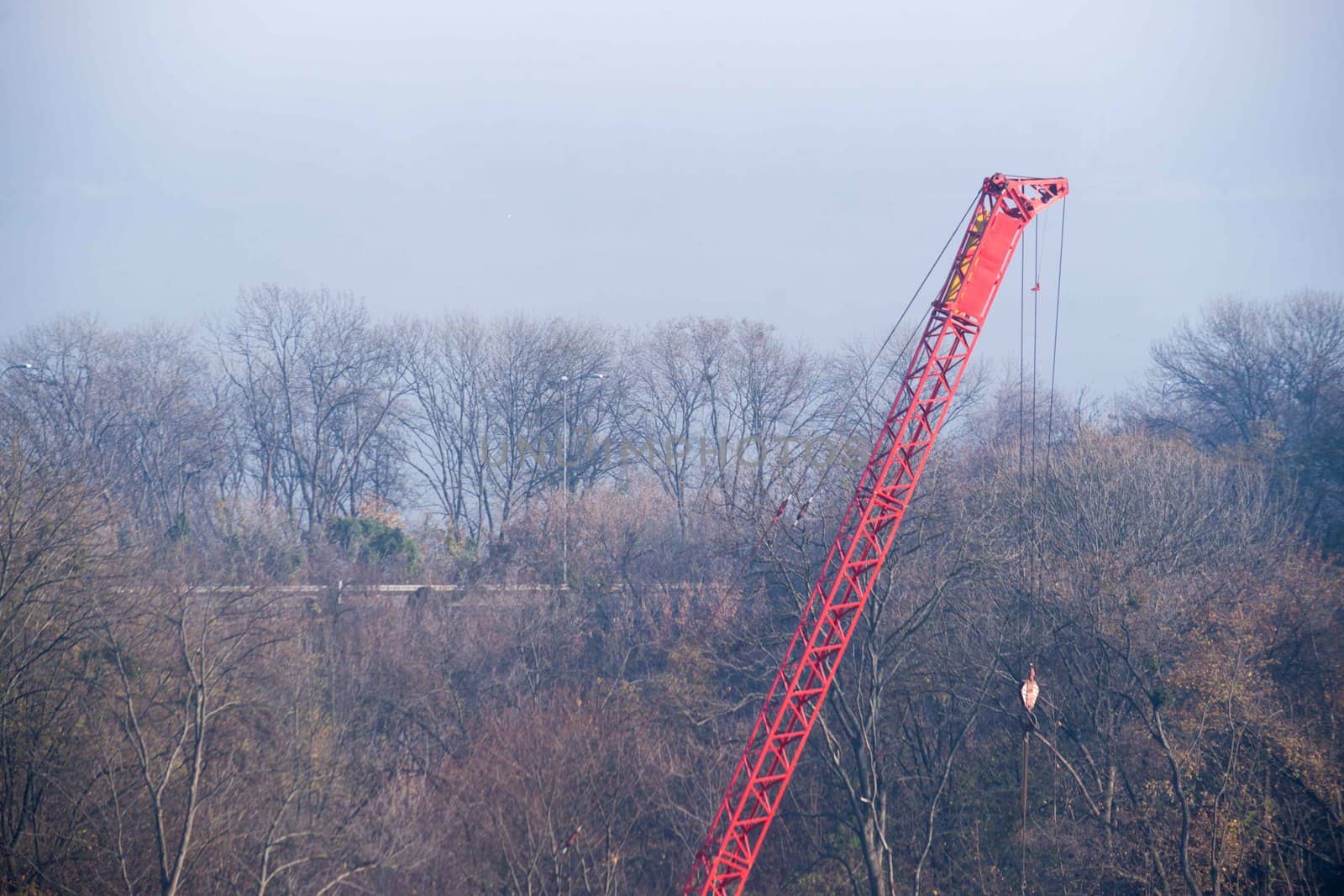 Construction process with construction automotive crane with red gibbet. Autumn fog and river bridge  on blurred background. Forest around crane.