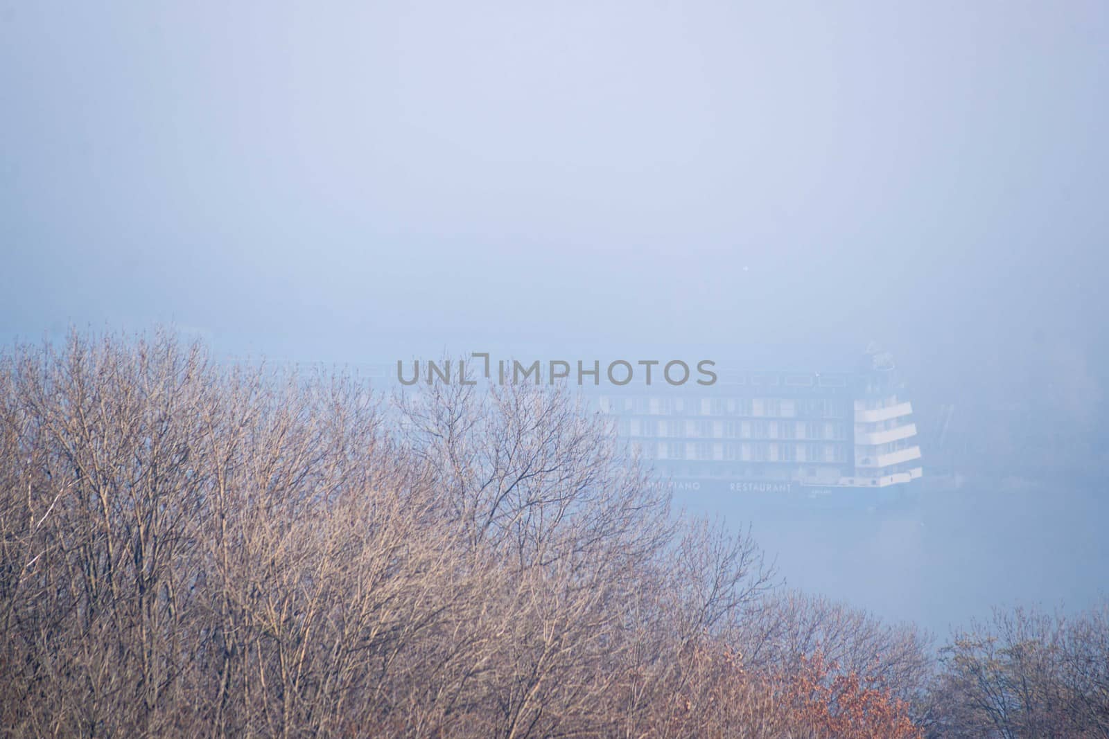 Autumn fog and big floating hotel in river on blurred background. Forest in foreground.