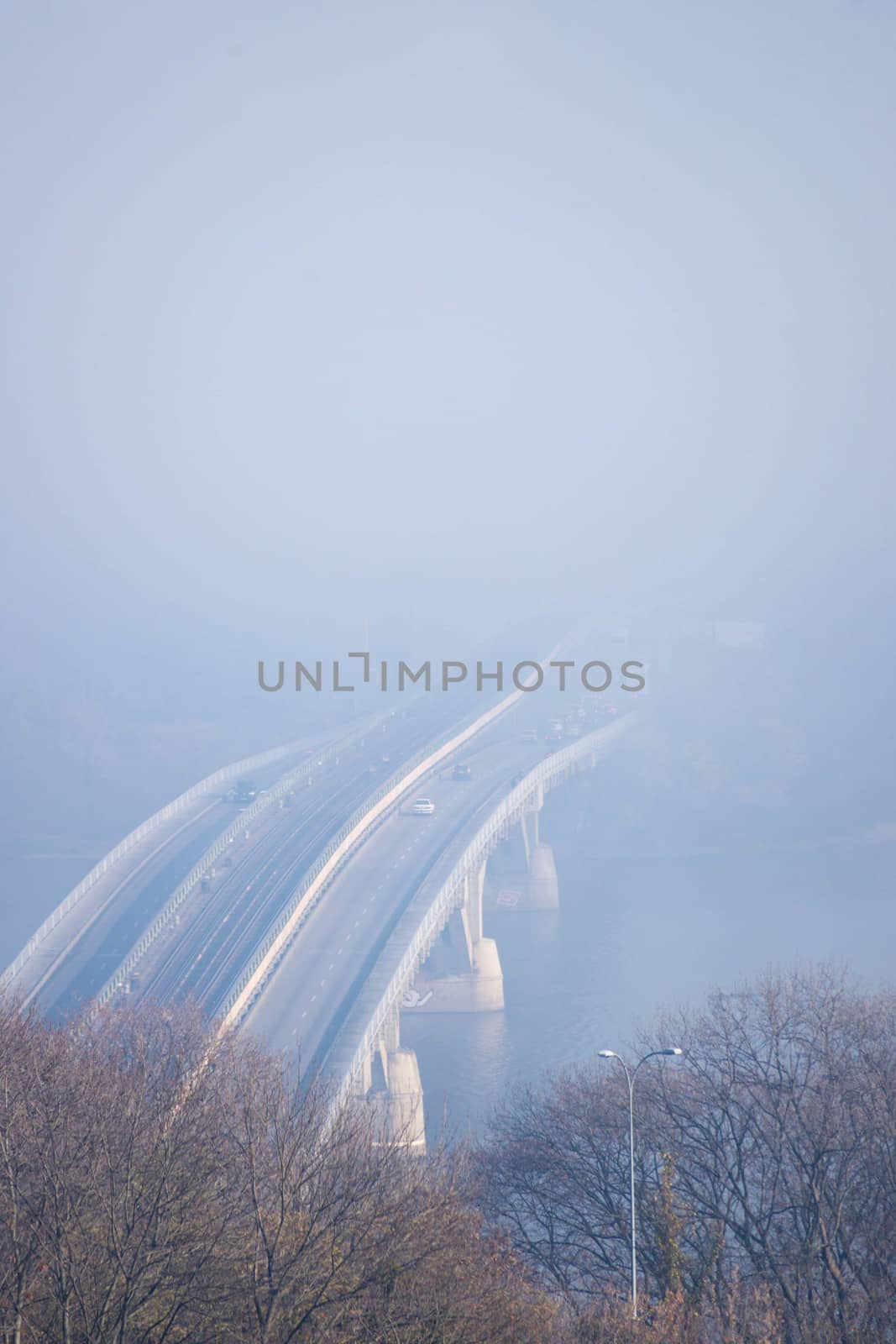 Autumn fog and river steel bridge with subway train on blurred background. Forest in foreground.